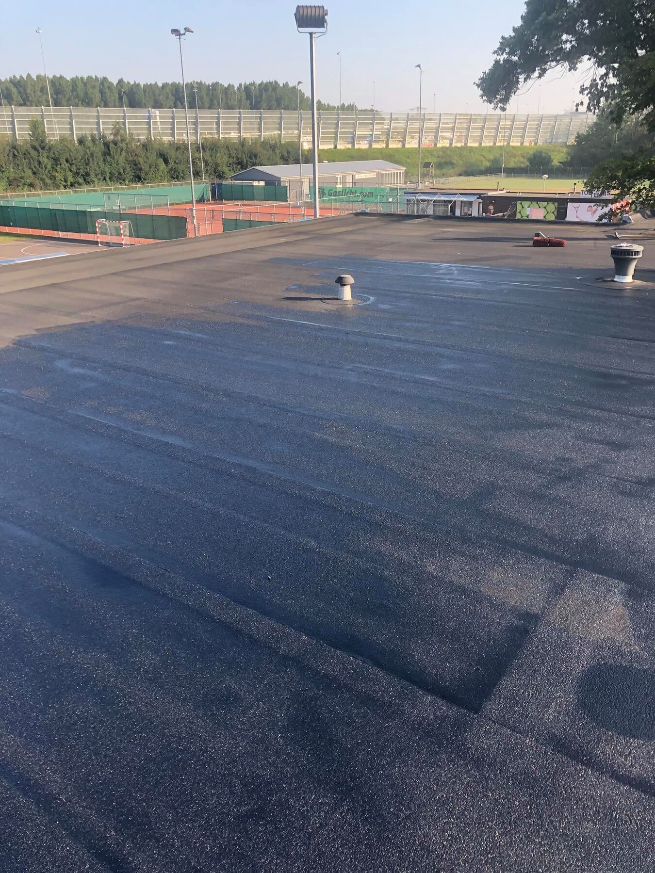 Nieuw bitumen dak van een clubgebouw, met sportvelden op de achtergrond